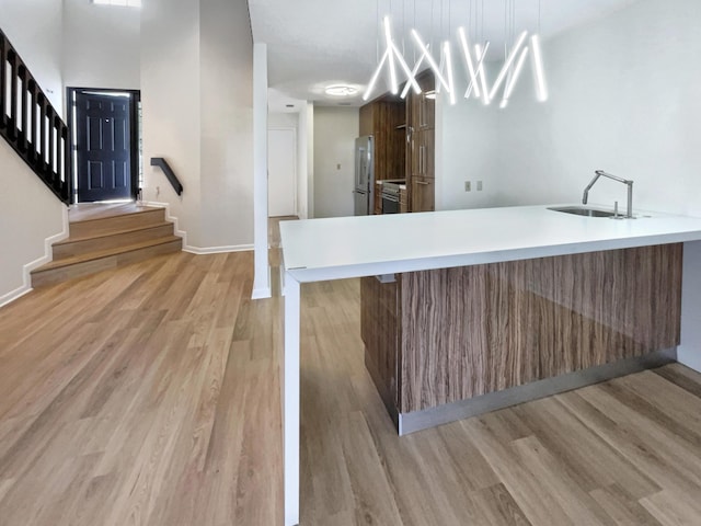 kitchen featuring kitchen peninsula, pendant lighting, light wood-type flooring, and stainless steel refrigerator