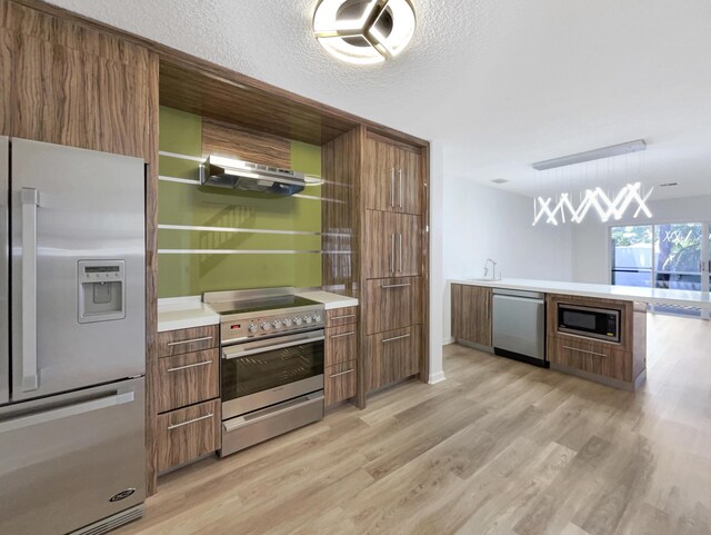 kitchen with light wood-type flooring, appliances with stainless steel finishes, ventilation hood, a textured ceiling, and hanging light fixtures