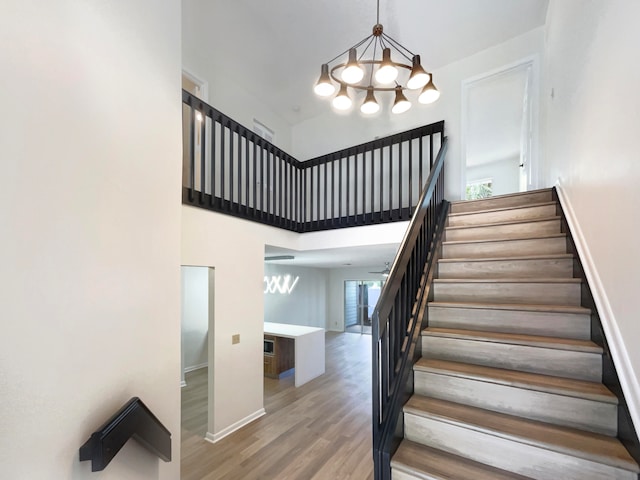 stairway featuring a wealth of natural light, a chandelier, hardwood / wood-style flooring, and a towering ceiling