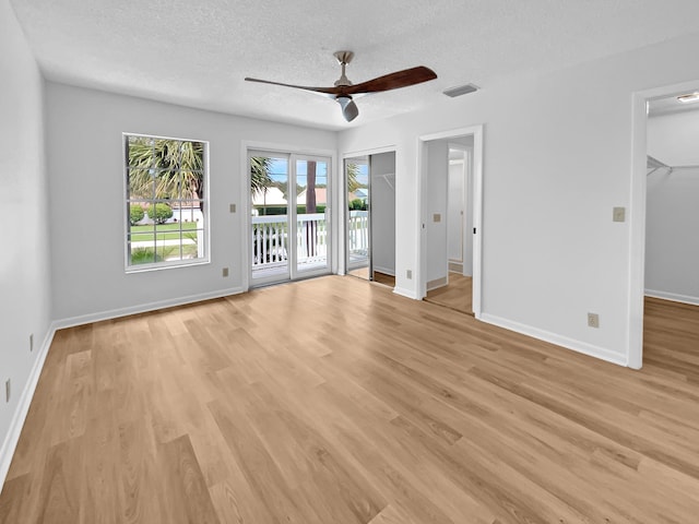 unfurnished bedroom featuring a walk in closet, light wood-type flooring, a textured ceiling, ceiling fan, and access to outside