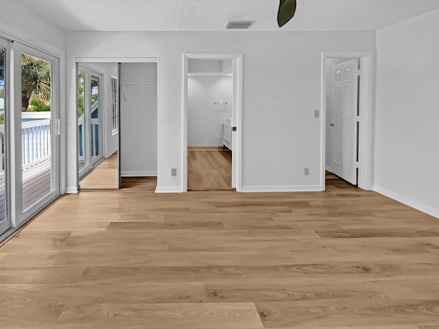 unfurnished bedroom featuring ensuite bath, a textured ceiling, light hardwood / wood-style floors, ceiling fan, and access to exterior