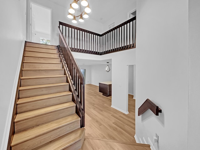 stairway featuring a chandelier, wood-type flooring, and a towering ceiling