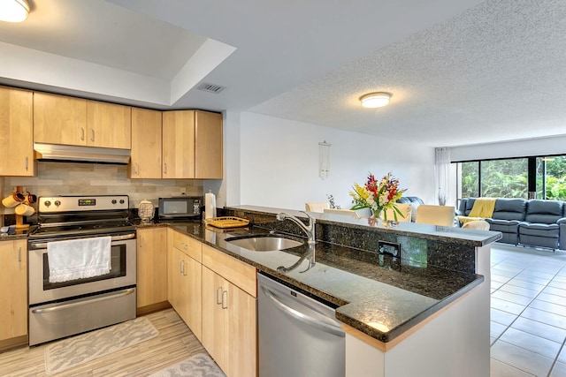 kitchen featuring sink, dark stone countertops, decorative backsplash, stainless steel appliances, and kitchen peninsula