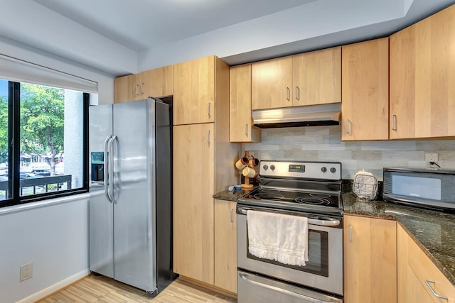 kitchen with appliances with stainless steel finishes, light brown cabinetry, light hardwood / wood-style floors, tasteful backsplash, and wall chimney range hood