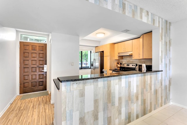 kitchen with backsplash, dark stone countertops, appliances with stainless steel finishes, light tile patterned floors, and kitchen peninsula