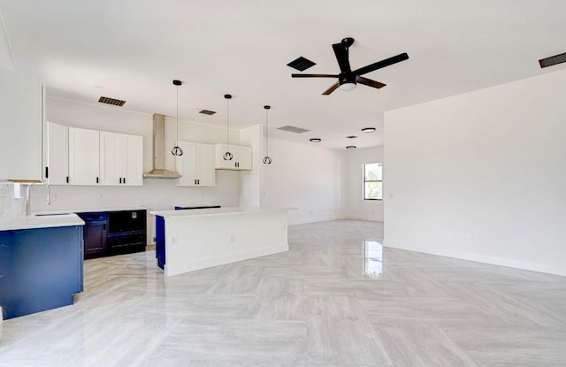 kitchen featuring a center island, sink, ceiling fan, wall chimney range hood, and white cabinets