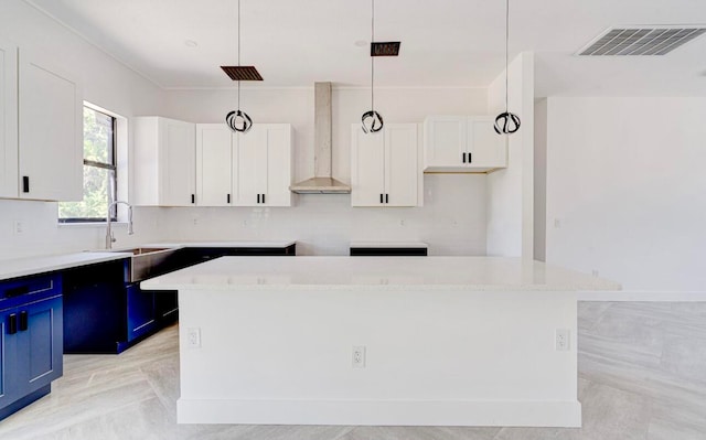 kitchen featuring light stone countertops, a kitchen island, white cabinetry, hanging light fixtures, and wall chimney range hood