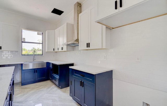 kitchen with wall chimney exhaust hood, tasteful backsplash, blue cabinetry, white cabinetry, and sink