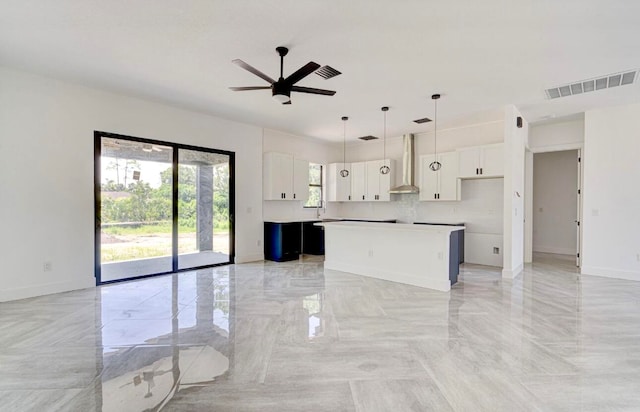 kitchen with a center island, wall chimney exhaust hood, ceiling fan, pendant lighting, and white cabinets