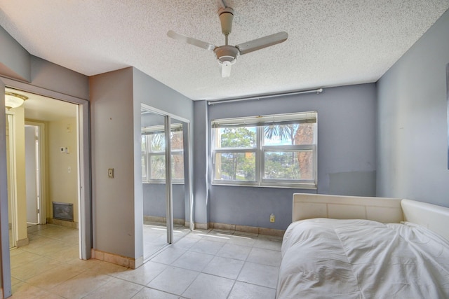 bedroom featuring ceiling fan, a closet, a textured ceiling, and light tile patterned flooring