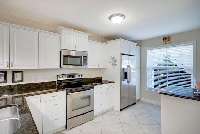 kitchen with stainless steel appliances, white cabinets, light tile patterned floors, and dark stone countertops