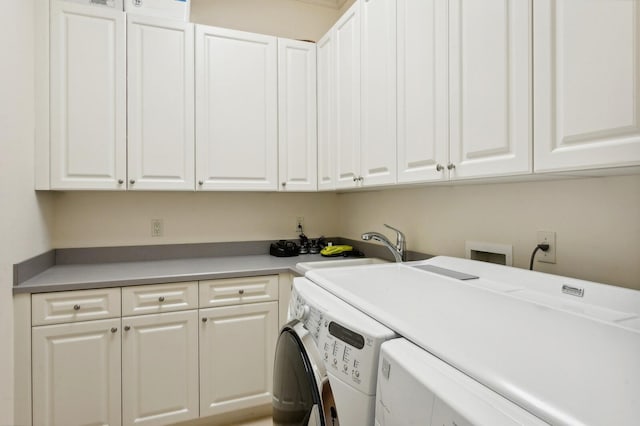 clothes washing area with washing machine and clothes dryer, cabinets, and sink