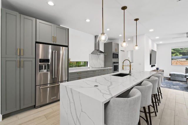 kitchen featuring a center island with sink, sink, appliances with stainless steel finishes, wall chimney exhaust hood, and gray cabinets