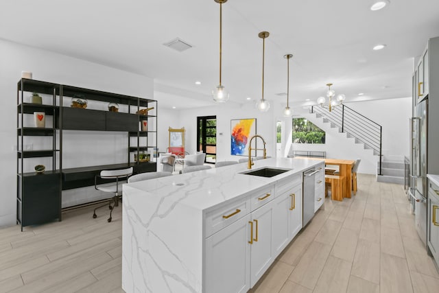 kitchen featuring pendant lighting, sink, a kitchen island with sink, light stone countertops, and white cabinetry