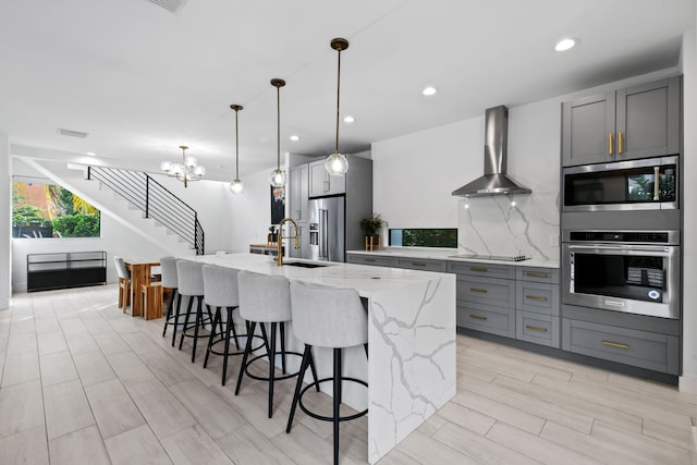 kitchen with wall chimney exhaust hood, gray cabinets, light stone countertops, a spacious island, and appliances with stainless steel finishes