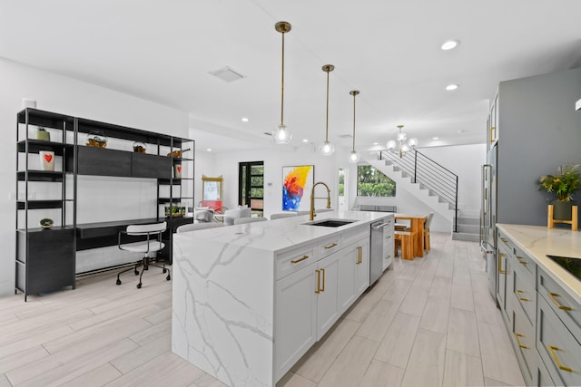 kitchen featuring a center island with sink, sink, light stone countertops, hanging light fixtures, and white cabinets