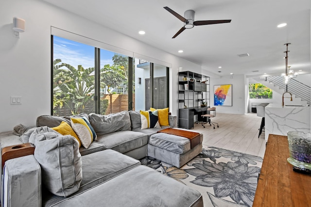 living room with light wood-type flooring and ceiling fan with notable chandelier