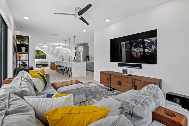 living room with ceiling fan with notable chandelier, sink, and light hardwood / wood-style flooring