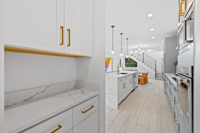 kitchen with stainless steel appliances, white cabinetry, light stone countertops, hanging light fixtures, and sink