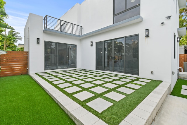 rear view of property with a balcony, a patio, and a yard