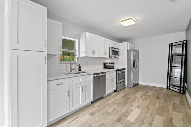 kitchen featuring stainless steel appliances, white cabinetry, decorative backsplash, sink, and light hardwood / wood-style flooring