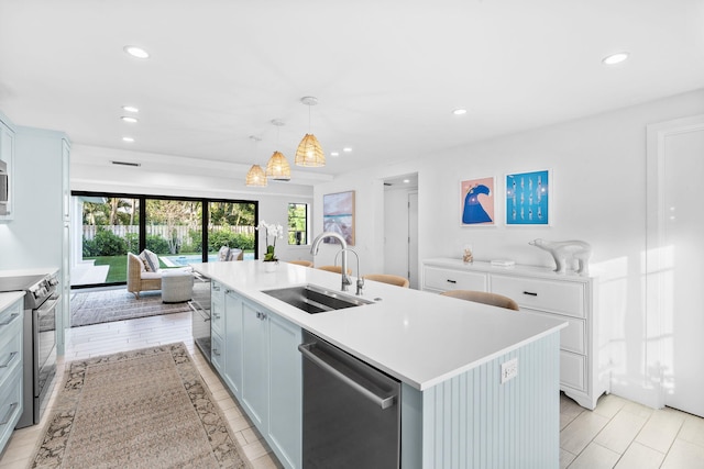 kitchen with sink, white cabinetry, hanging light fixtures, stainless steel appliances, and an island with sink