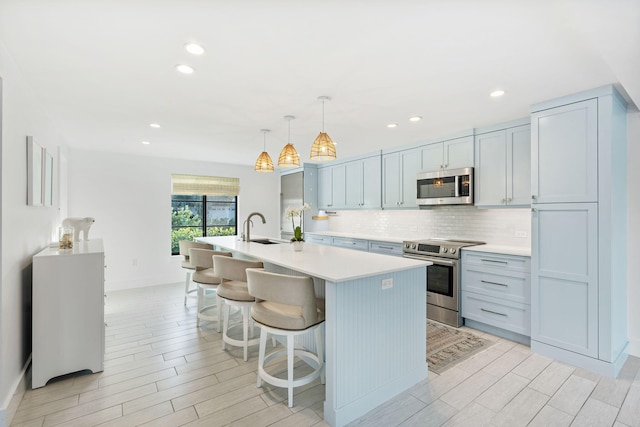 kitchen with sink, a breakfast bar, appliances with stainless steel finishes, hanging light fixtures, and an island with sink