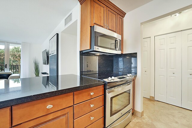 kitchen with dark stone counters, stainless steel appliances, light tile patterned flooring, and tasteful backsplash