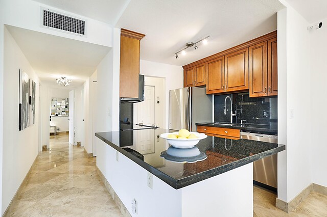 kitchen with sink, dark stone countertops, rail lighting, tasteful backsplash, and stainless steel appliances