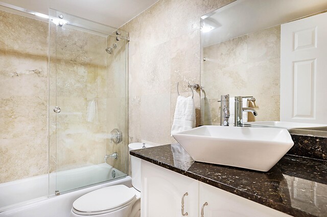 full bathroom featuring tile walls, toilet, vanity, and enclosed tub / shower combo