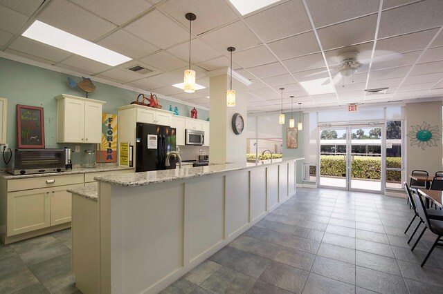 kitchen featuring ceiling fan, a kitchen island with sink, black refrigerator, and a paneled ceiling