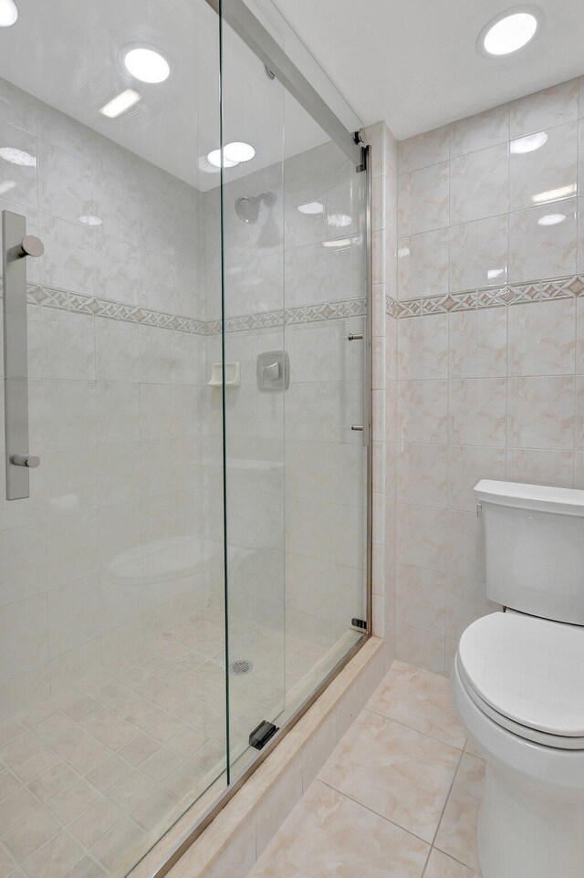 bathroom featuring tile walls, toilet, and a shower with shower door