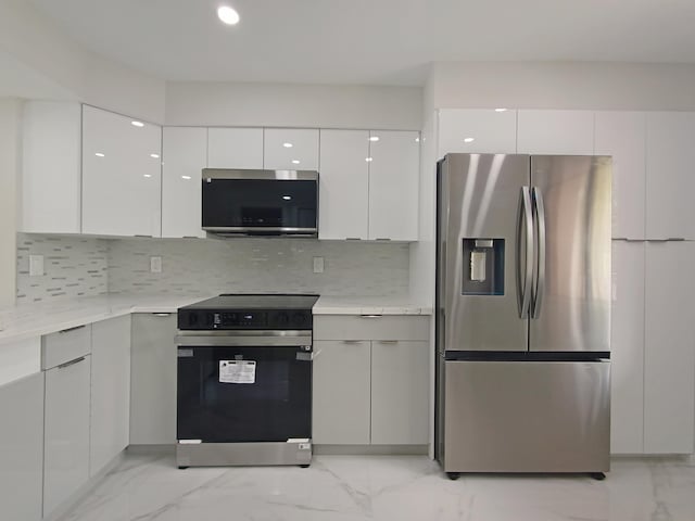 kitchen featuring appliances with stainless steel finishes, white cabinetry, light stone counters, and tasteful backsplash