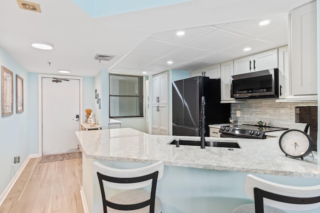 kitchen with backsplash, light hardwood / wood-style floors, white cabinetry, black refrigerator, and range with electric stovetop