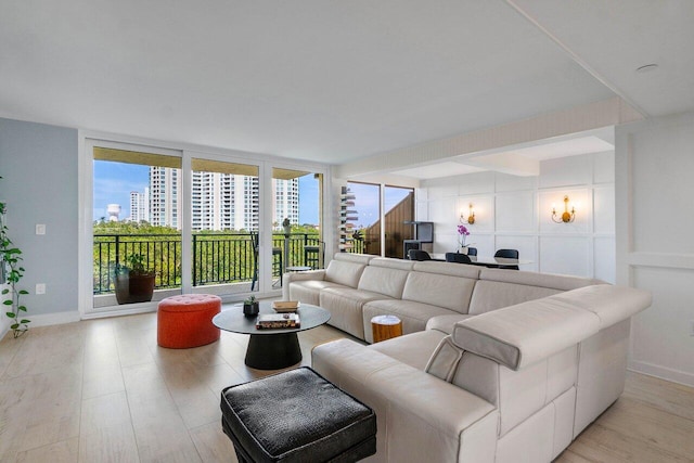 living area featuring expansive windows, baseboards, light wood finished floors, and a view of city