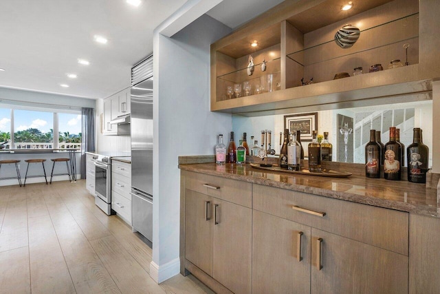 bar with a bar, under cabinet range hood, stainless steel appliances, and light wood finished floors