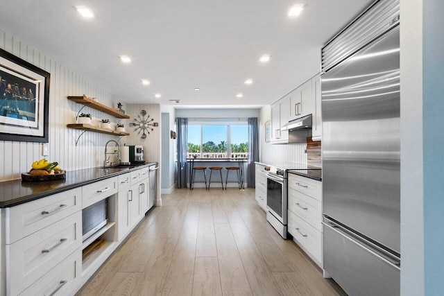 kitchen with under cabinet range hood, a sink, stainless steel appliances, and dark countertops