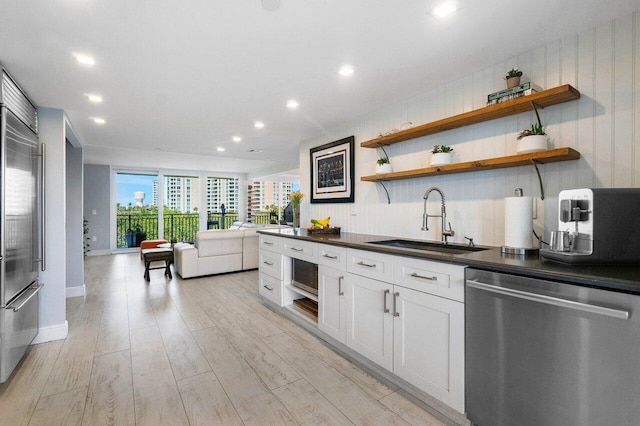 kitchen with a sink, open floor plan, light wood-type flooring, stainless steel appliances, and dark countertops