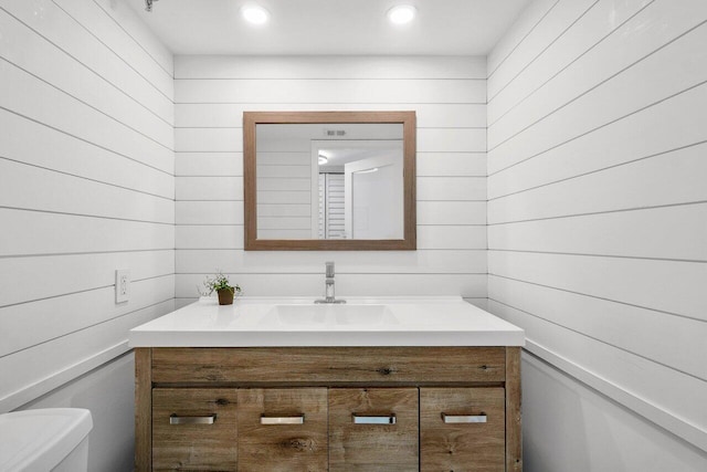 bathroom featuring wooden walls, vanity, and toilet