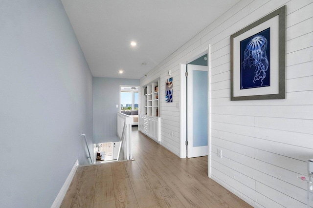 corridor with an upstairs landing, wood walls, baseboards, and wood finished floors