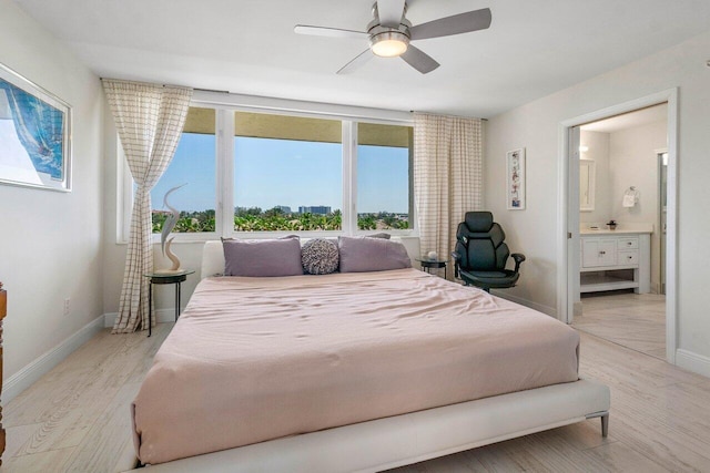 bedroom featuring connected bathroom, baseboards, light wood-style flooring, and a ceiling fan