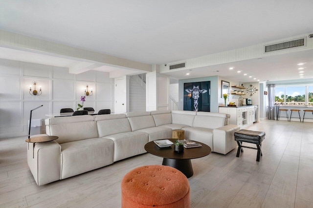 living room featuring stairs, a decorative wall, visible vents, and light wood-style floors