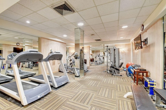 exercise room with a paneled ceiling, carpet, and wooden walls