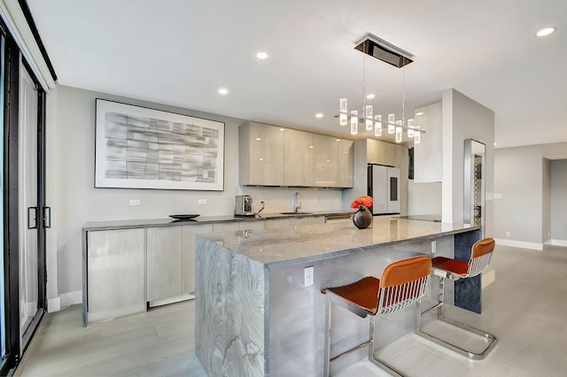 kitchen with a kitchen breakfast bar, dark stone counters, sink, white fridge, and hanging light fixtures