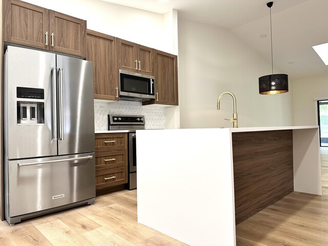 kitchen with decorative light fixtures, appliances with stainless steel finishes, light hardwood / wood-style floors, sink, and decorative backsplash