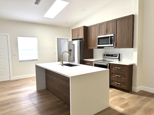 kitchen with appliances with stainless steel finishes, light hardwood / wood-style floors, a kitchen island with sink, and sink