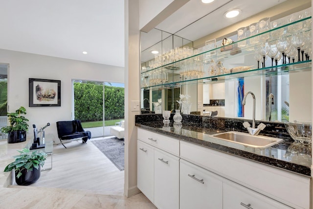 bar with sink, light hardwood / wood-style flooring, white cabinets, and dark stone counters