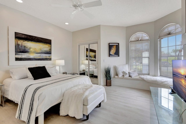 bedroom featuring a textured ceiling, ceiling fan, multiple windows, and light wood-type flooring