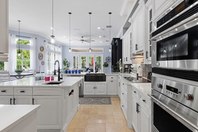 kitchen featuring sink, white cabinets, decorative light fixtures, and an island with sink