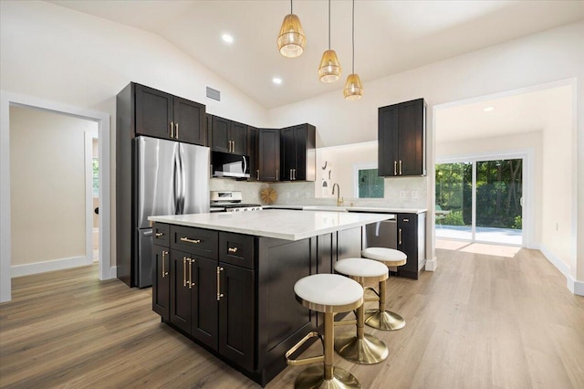 kitchen featuring an inviting chandelier, vaulted ceiling, stainless steel appliances, light hardwood / wood-style floors, and a kitchen island